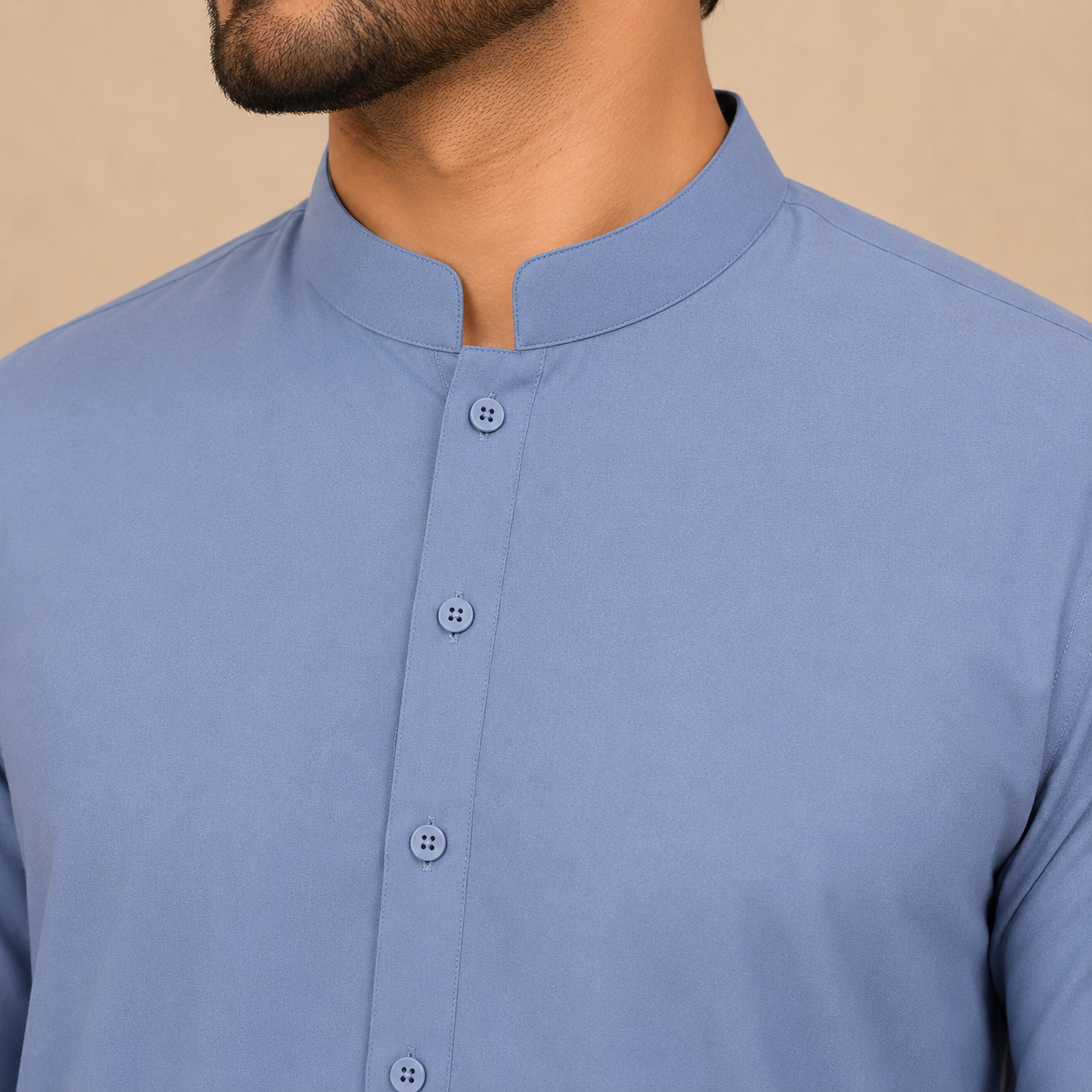 A close-up of a man wearing a light blue, mandarin-collar button-up shirt against a solid beige background.