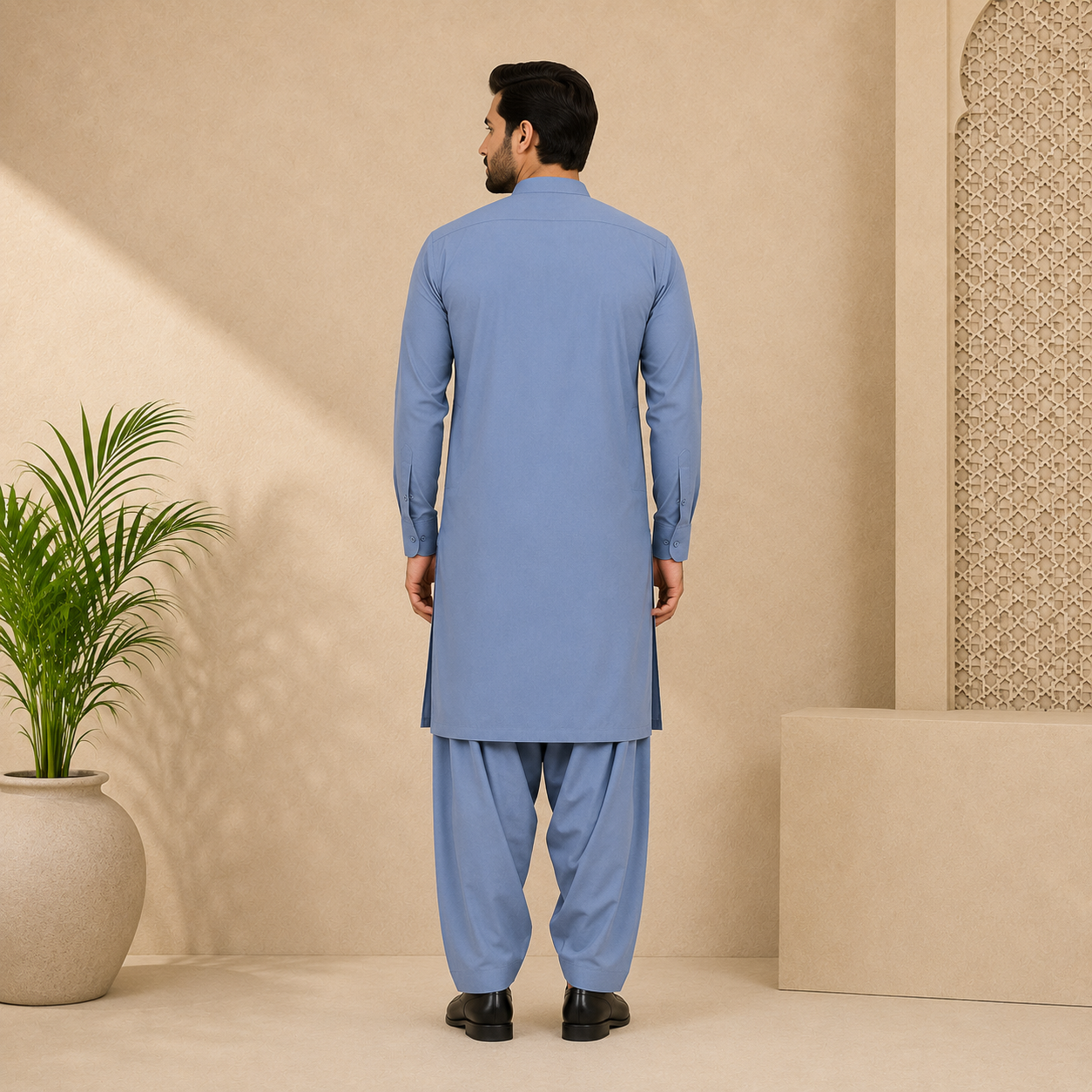 A man viewed from the back wearing a light blue traditional kurta and matching pants, standing in a beige studio setting with a potted plant on the left.