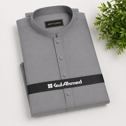 A folded gray long-sleeve shirt with a mandarin collar and silver buttons, featuring a black waist strap with the brand name 'GulAhmed' in white. The shirt is displayed on a light gray background with a green plant in the top right corner.