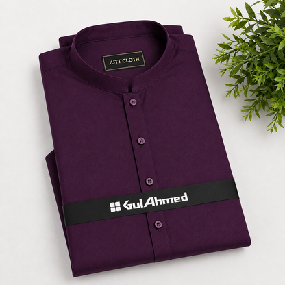A folded dark purple kurta shirt with a mandarin collar and button front, displayed on a white background with a green plant leaf in the corner. The shirt features a black waistband with the white printed brand name 'GulAhmed'.
