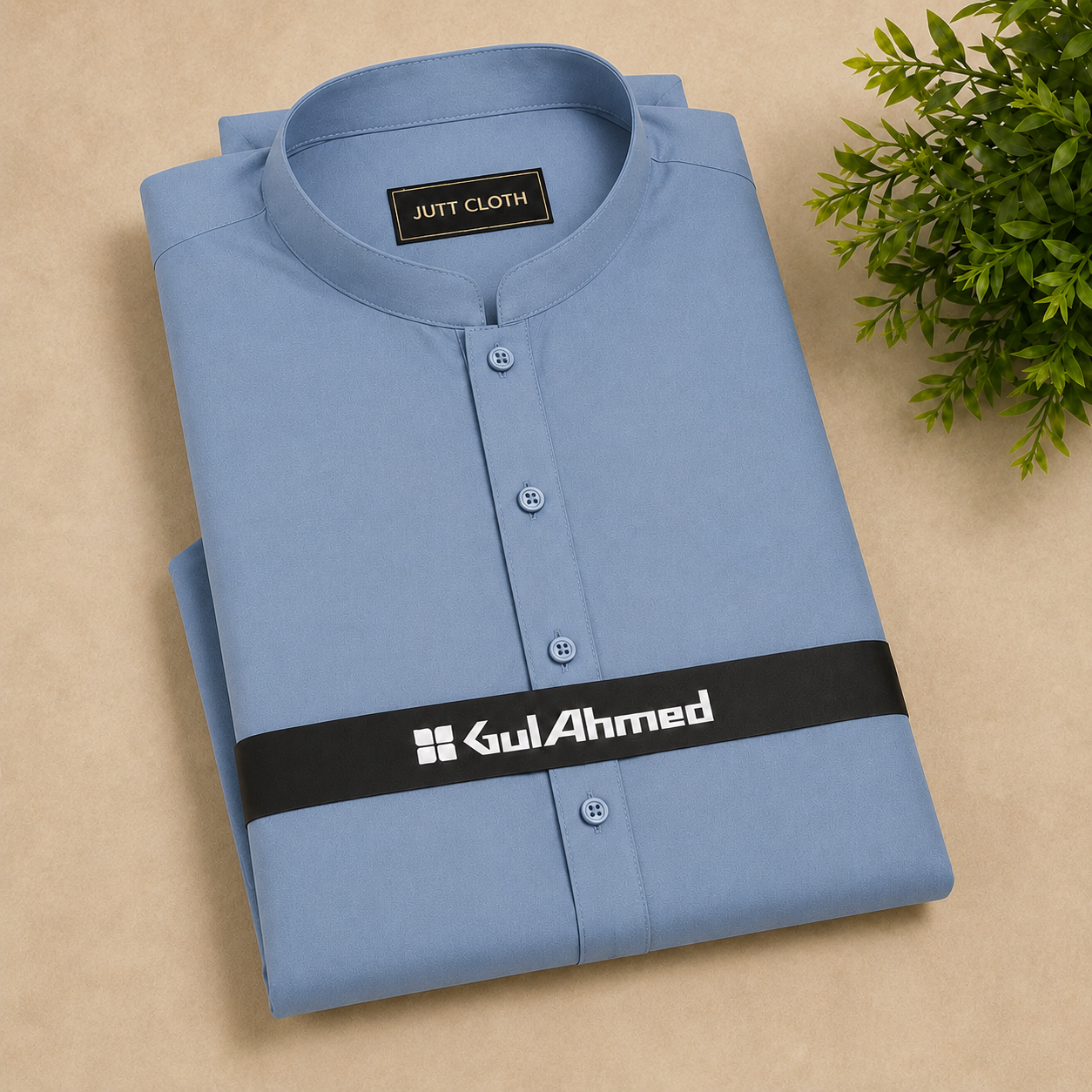 A folded light blue men's shirt with a mandarin collar and button placket, displayed on a beige surface with a small green plant in the corner. The shirt features a black brand band with 'GulAhmed' printed in white.