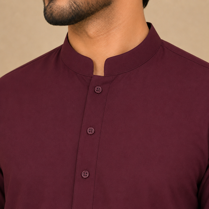 Close-up of a man wearing a maroon stand-collar kurta with three front buttons, cropped from the chin down against a plain beige background.